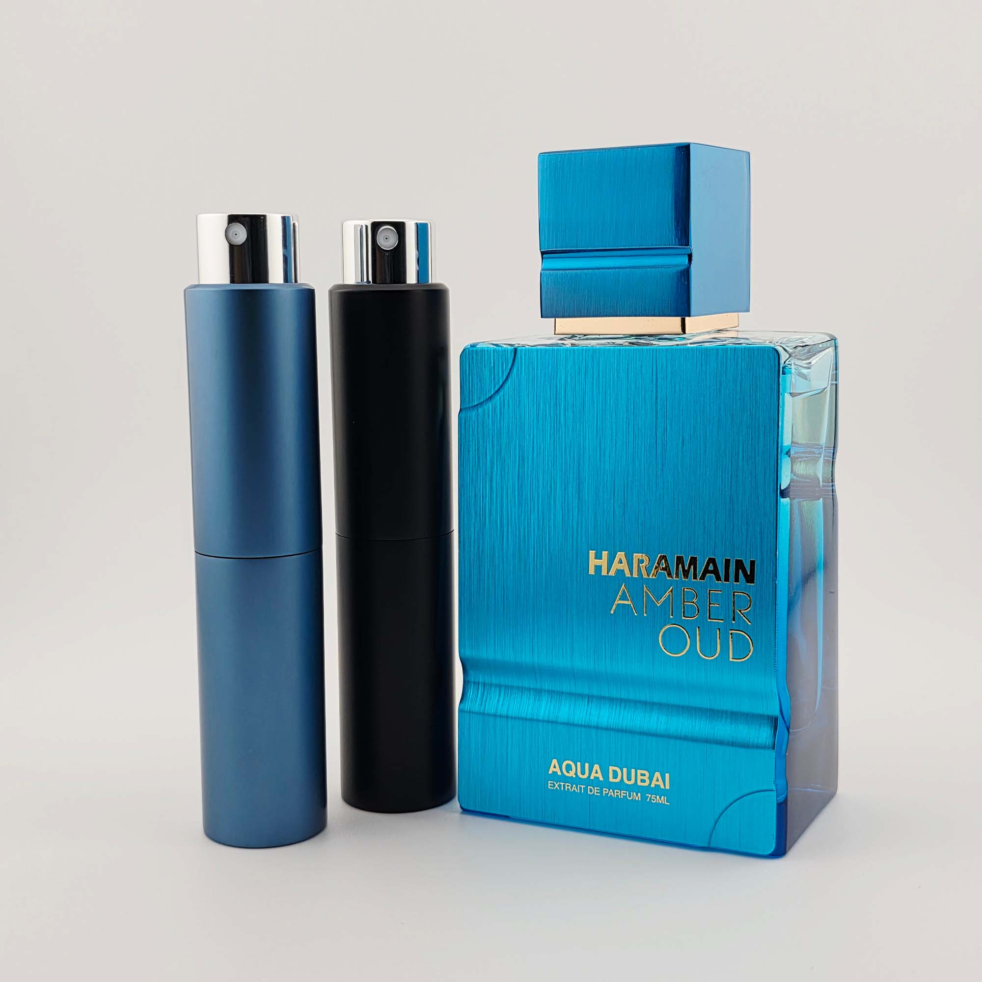 Al Haramain Amber Oud Aqua Dubai with two travel-size decant atomizers on a plain background