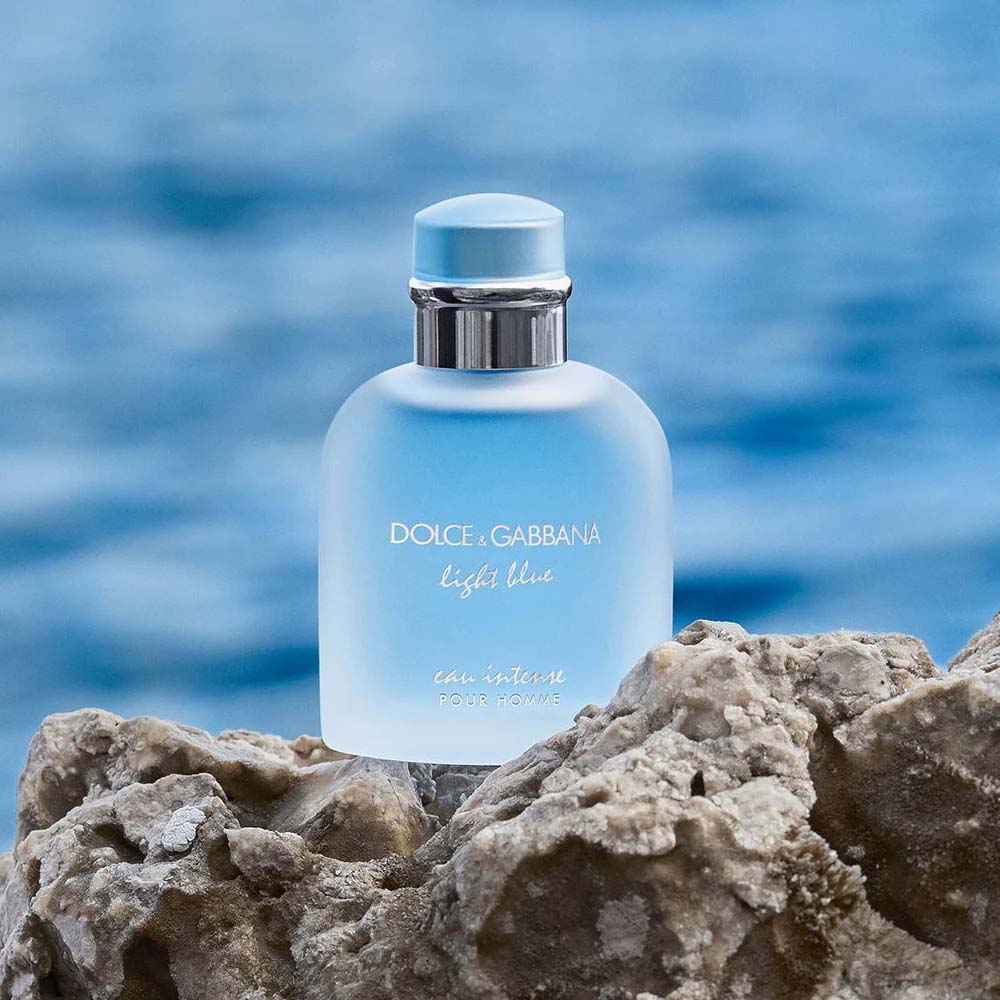Dolce & Gabbana Light Blue Eau Intense Pour Homme bottle on rocky shore with ocean background