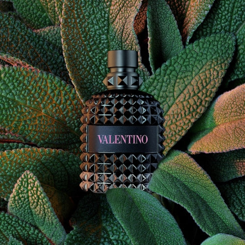 Valentino Uomo Born In Roma EDT bottle surrounded by lush green textured leaves, showcasing the fragrance in a natural setting.
